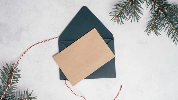 Green open envelope on white concrete background with blank kraft paper greeting card with branches of Christmas tree. New year envelope with untied cord. Copy space. Top view