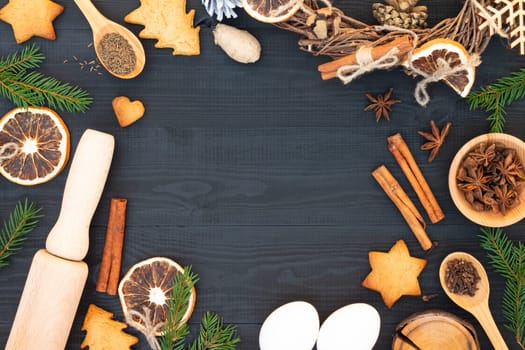 Christmas tree branches, gingerbread cookies, spices and baking supplies on black wood background. Christmas, New Year greeting card