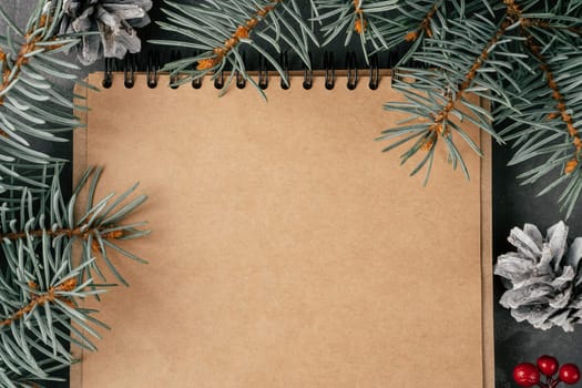 Happy New Year. Open brown kraft paper folded notebook on spring with Christmas tree branches and pine cones. Merry Christmas. Top view. Copy space