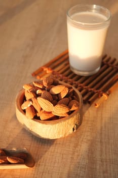 A bowl of almonds sits beside a glass of milk on a wooden surface.