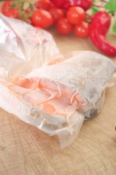 Fish is wrapped in parchment paper, surrounded by fresh vegetables and herbs.