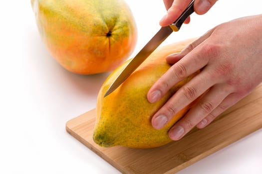 Kitchen knife positioned for a first cut through a papaya along its longitudinal axis. The left hand of a chef is placing the tropical fruit on a cutting board, while his right is guiding the blade.