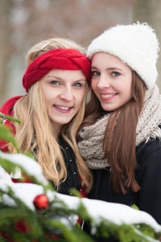 Two girlfriends outside in front of a Christmas tree in winter