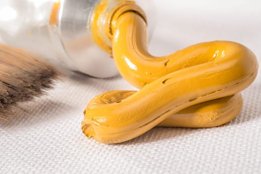 A Yellow Ochre oil paint paste is pressed from a tube on to a white canvas.
