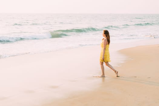 Goa, India. Young Caucasian Woman In Yellow Dress Go To Sea Ocean And Looking Into Distance.