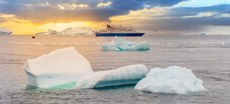 blue expedition ship in front of antarctic iceberg landscape in Cierva Cove - a deep inlet on the west side of the Antarctic Peninsula, surrounded by dramatic glacier fronts