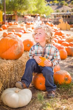 Little Boy Sitting and Holding His Pumpkin in a Rustic Ranch Setting at the Pumpkin Patch.