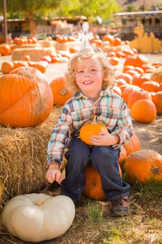 Little Boy Sitting and Holding His Pumpkin in a Rustic Ranch Setting at the Pumpkin Patch.