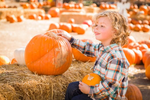 Little Boy Sitting and Holding His Pumpkin in a Rustic Ranch Setting at the Pumpkin Patch.