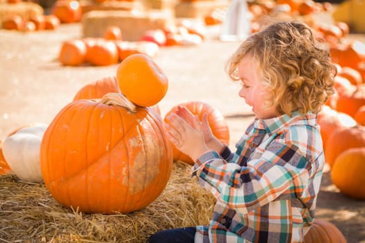 Little Boy Sitting and Holding His Pumpkin in a Rustic Ranch Setting at the Pumpkin Patch.