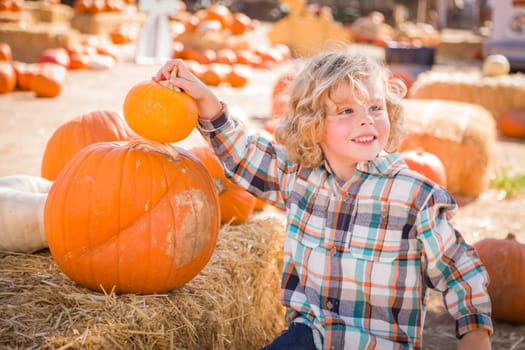 Little Boy Sitting and Holding His Pumpkin in a Rustic Ranch Setting at the Pumpkin Patch.