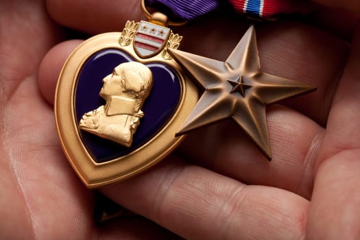 Man Holding Purple Heart and Bronze War Medals in The Palm of His Hand.
