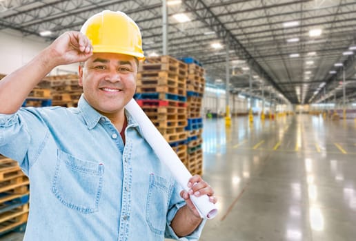 Hispanic Male Contractor Wearing Hard Hat Standing in Empty Industrial Warehouse.