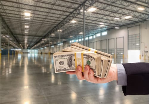 Male Hand Holding Thousands of Dollars Inside Empty Industrial Warehouse.