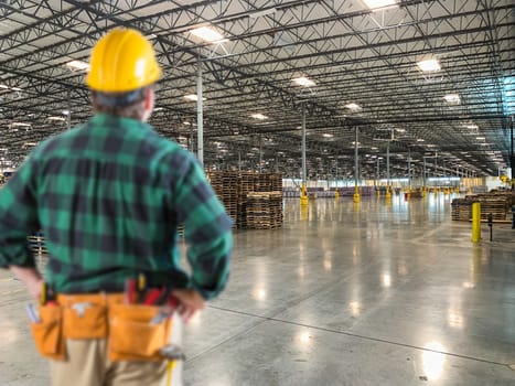 Male Contractor Wearing Hard Hat Standing in Empty Industrial Warehouse.