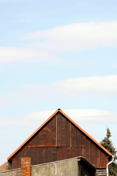 The roof of a barn and of stables of a farm in front of a light blue sky.