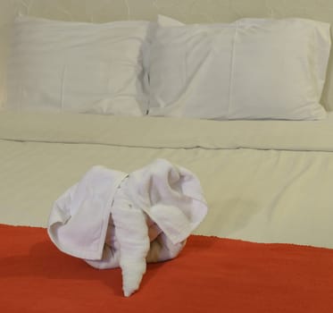 White towel in elephant shape on white bed in Thai style hotel bedroom