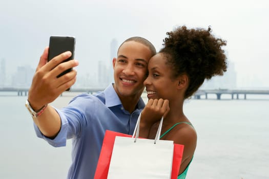 Black tourist heterosexual couple in Casco Antiguo Panama City with shopping bags. The man takes a selfie with his girlfiend and shopping bags with skyline in background