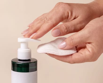A woman hand pumping liquid on a make-up remover pad from a cosmetic bottle on beige close up. Skincare beauty product package, minimal composition..
