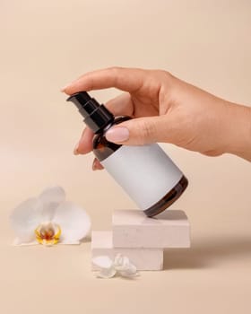 A woman hand pumping liquid from a cosmetic bottle near orchid flowers on beige close up, label mockup. Skincare beauty product package, minimal composition..