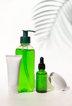 Refillable Cosmetic bottles, jar and tube with green liquid on white, Palm leaf hard shadows, close up, mockup. Skincare beauty products. Natural cosmetics with aloe vera..