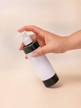 A woman hand pumping disinfectant liquid from a bottle with blank label on light beige, close up, mockup. Health protection concept. Skincare beauty product package, minimal composition..