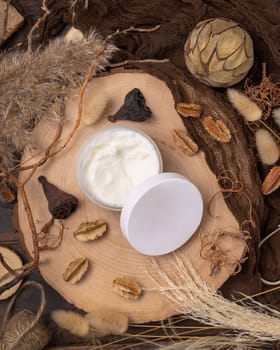 Opened cream jar with blank lid on wood near natural decorations top view, package mockup. Eco friendly skincare product, lotion or cream. Bohemian composition with dried leaves and flowers.