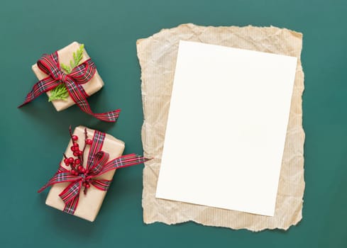 Blank paper card and wrapped Christmas presents on a green background top view. Holidays winter mockup, copy space. New Year and Christmas holiday atmospheric flat lay