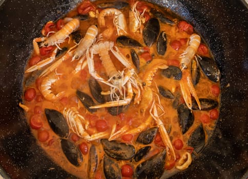 Cooking Italian stew with seafood and tomatoes in a big frying pan top view. Mediterranean Apulian traditional food with fresh stewed clams, shrimps, mussels, octopus and squid