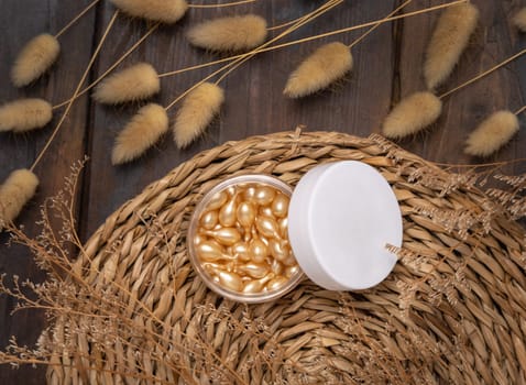 Beauty serum capsules in an opened jar with blank lid on wattled boho placemat near Hare's Tail grass top view. Skincare product for everyday beauty routine. Bohemian eco friendly cosmetics