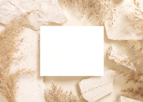Blank card near beige travertine stones and dried pampas grass top view, mockup. Boho scene with horizontal card. Bohemian or close to nature greeting or wedding Invitation. Close to nature.