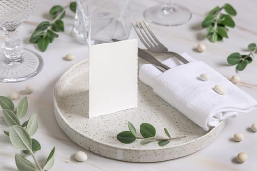 Elegant Table setting with a folded card decorated with eucalyptus branches close up, Wedding Mockup. Romantic table with blank card. Close to nature and simplicity concepts