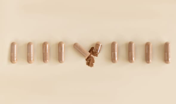 Medical capsules in a line on light beige top view, one capsule opened to show brown powder. Preventive medicine and healthcare, dietary supplements and vitamins