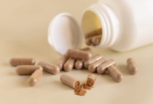 Medical capsules on light beige close up. One capsule opened to show brown powder. Preventive medicine and healthcare, taking dietary supplements and vitamins. Pharmaceutical product