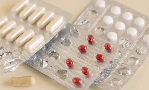 Mix of pills and capsules in a aluminum and plastic blisters with some missing pills already used on light beige close up. Preventive medicine and healthcare, taking dietary supplements and vitamins