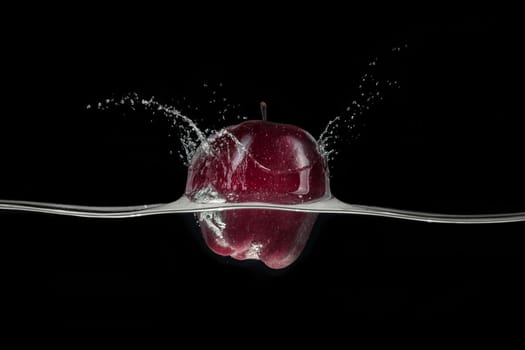 Red apple splashing in water, viewed from a side on black background.