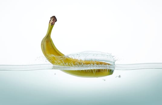 Banana splashing into water, viewed from a side on white background.