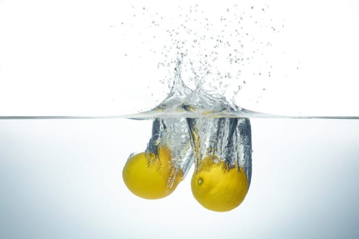 Two lemons splashing in clear water. Side view on white background.