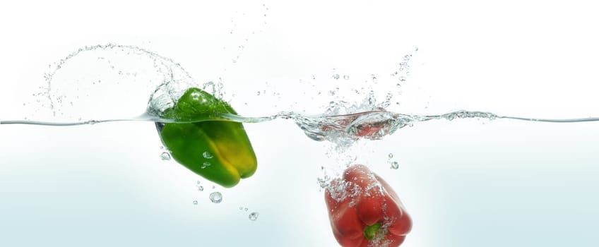 Two peppers green and red splashing in water. Side view on white background.