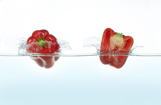 Two red peppers splashing in water. Side view on white background.