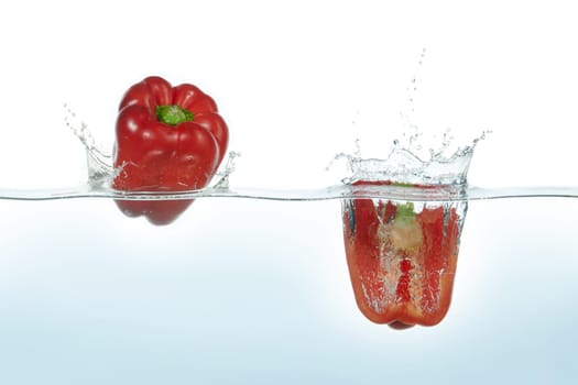Two red peppers splashing in water. Side view on white background.