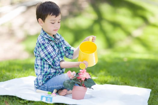 Mixed Race Young Boy Watering His Potted Flowers Outside On The Grass