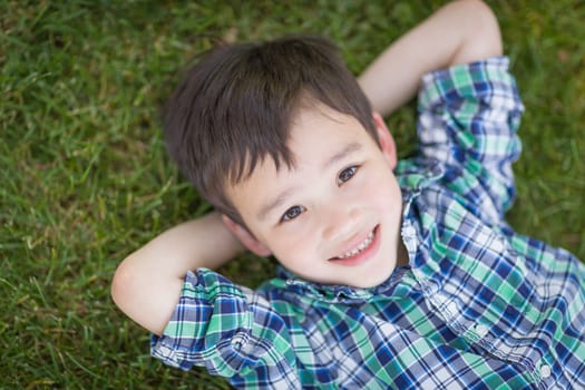 Mixed Race Chinese and Caucasian Young Boy Relaxing On His Back Outside On The Grass