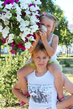 daughter sitting on her mother and many flowers in the city park