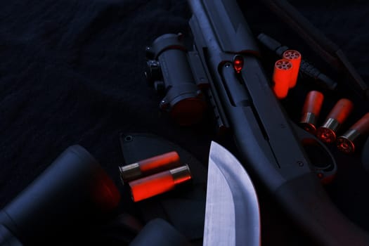 Weapon on black cloth: binoculars, flashlight, knife, rifle, shells,top view. Top view of knife rifle shells