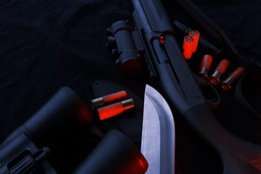 Weapon on black cloth: binoculars, flashlight, knife, rifle, shells,top view. Top view of knife rifle shells