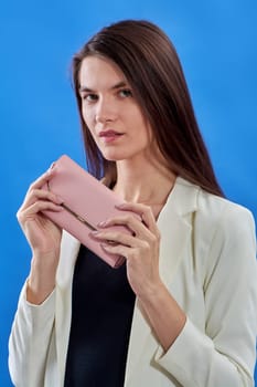 A beautiful young woman is holding a pink purse on a blue background, copy space. High quality photo