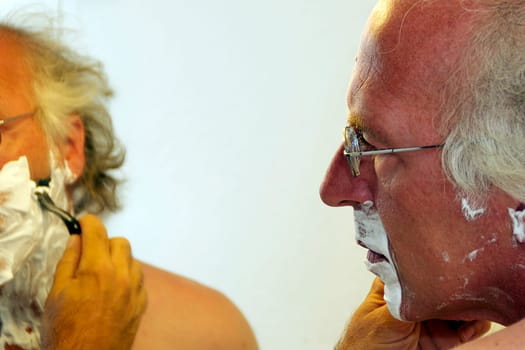 Profile on man looking in mirror while shaving his face.