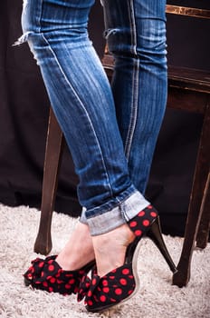 Legs of a young woman wearing high heels and blue jeans posing with a wooden chair