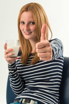 Smiling young girl holding a glass of milk sitting on a blue couch, top thumb and white background